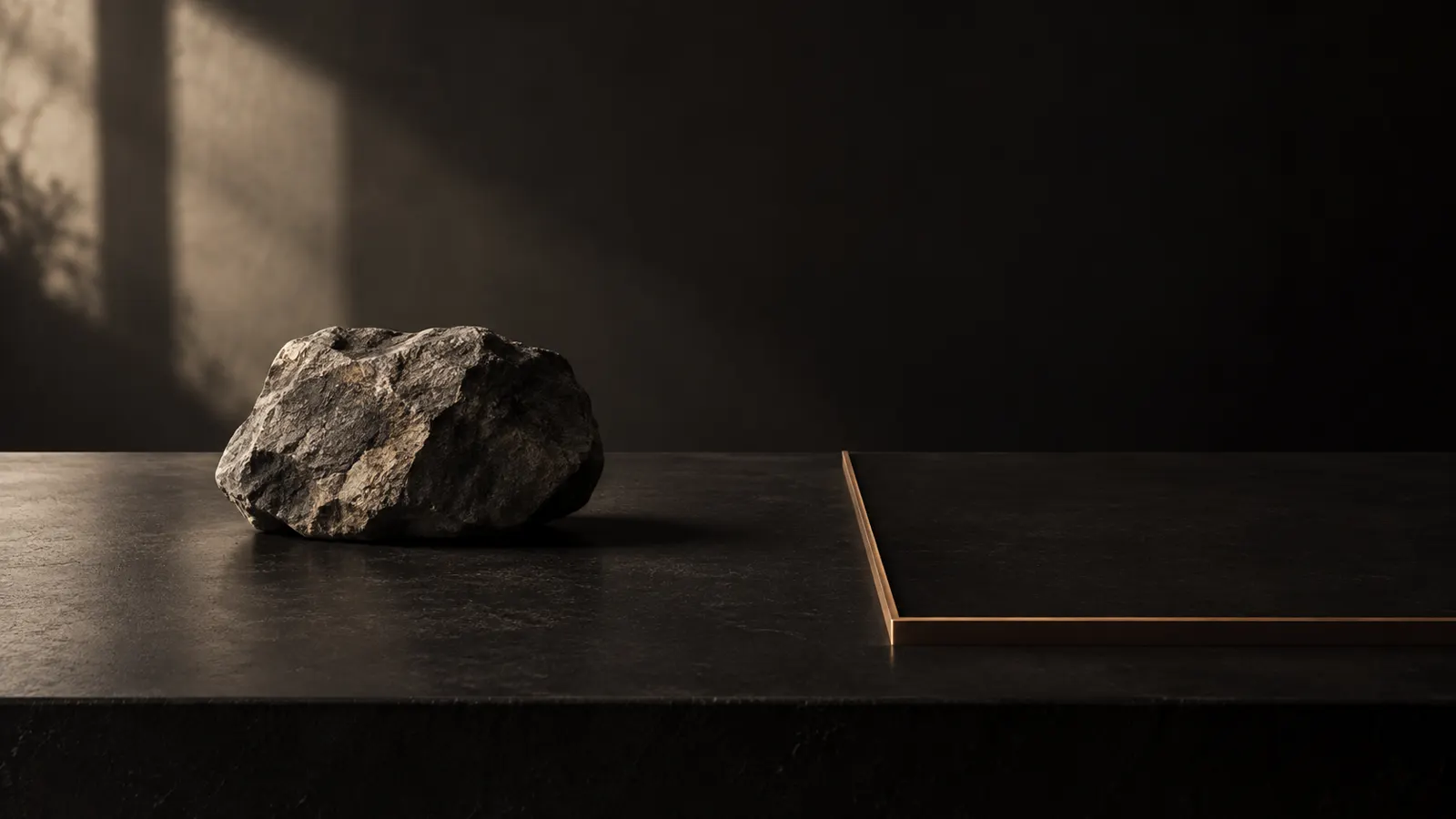 A rough gray stone on a dark surface next to a thin bronze border delimiting an empty space.